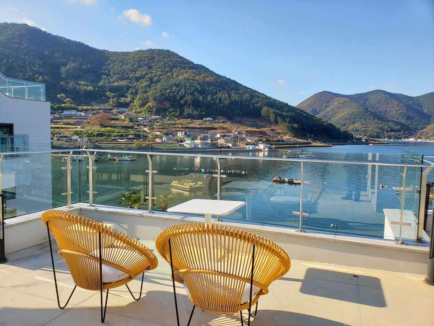 A pair of chairs on a balcony overlooking sheltered sea and mountains with a small town at the base in Korea