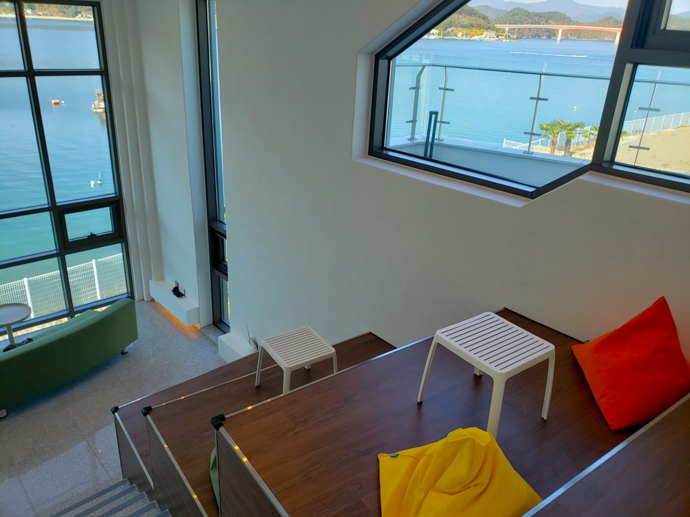Seating on the sides of the stairs inside a café with colorful pillows and a beautiful view out the large front-facing window