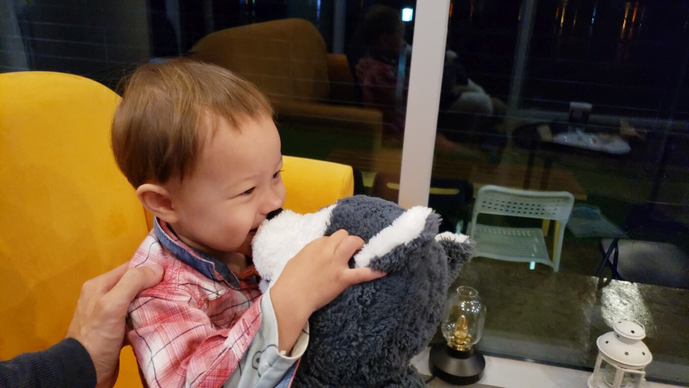Baby Noah kissing a stuffed animal on a couch in An Café