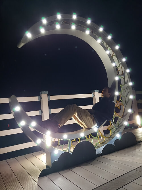 Nate laying on a moon-shaped structure with lights at night