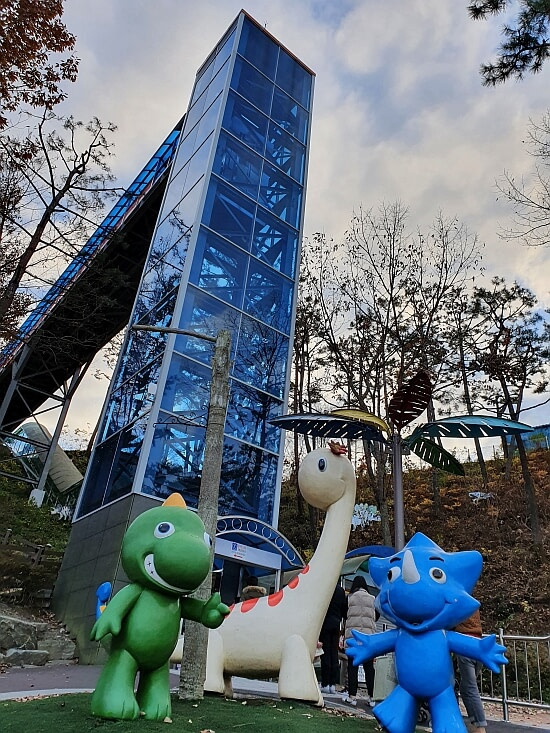 Two small kid-sized dinosaurs in front of an elevator that goes up to the Dinosaur Expo Pavilion
