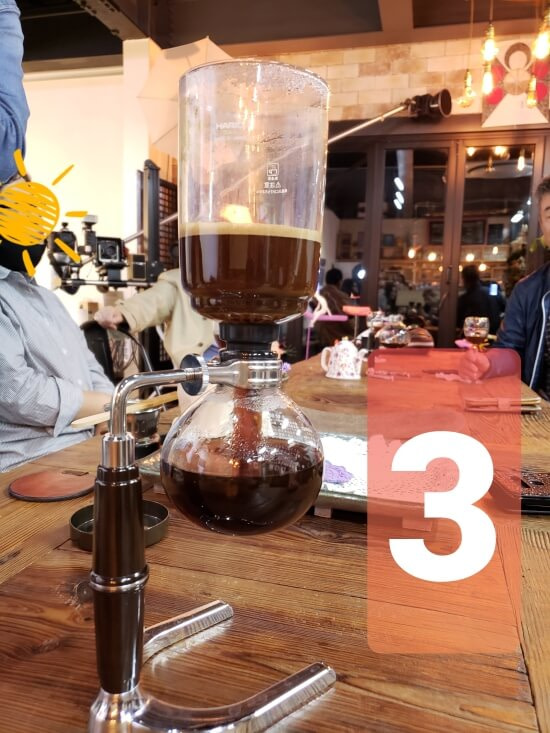 A siphon filled with hot coffee sinking back down into a lower glass chamber