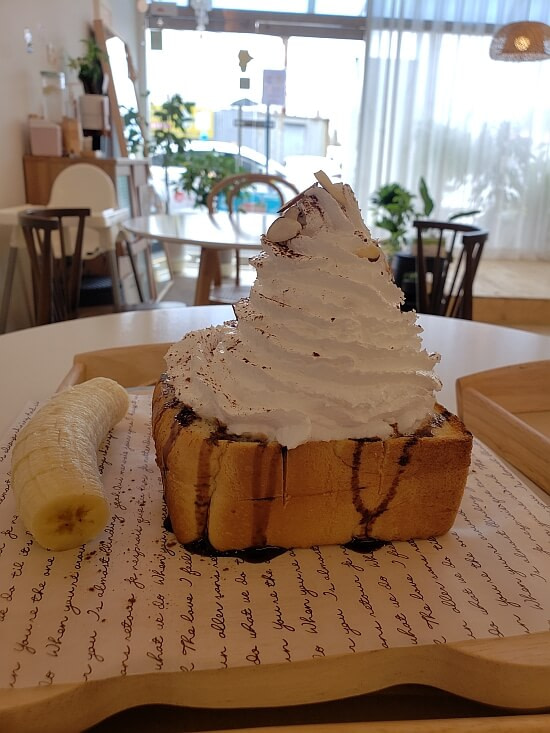 A tall pile of cream on a square piece of toast and a side of cut banana on a tray