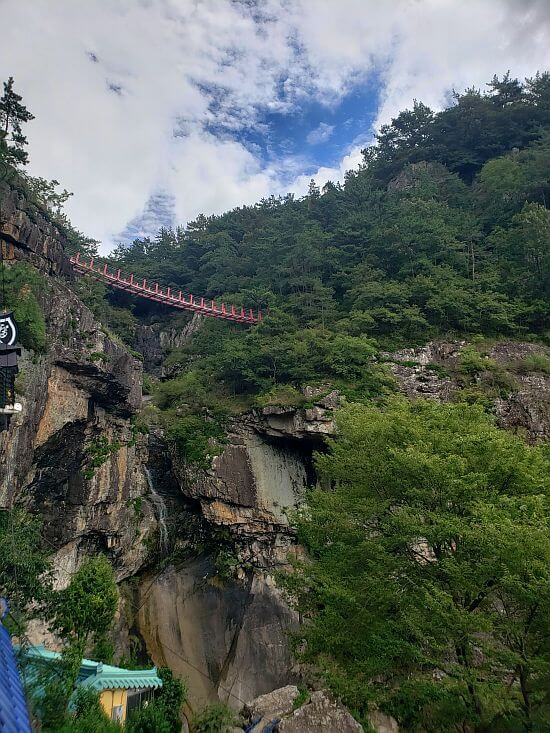 A red bridge across a rocky crevice and waterfall