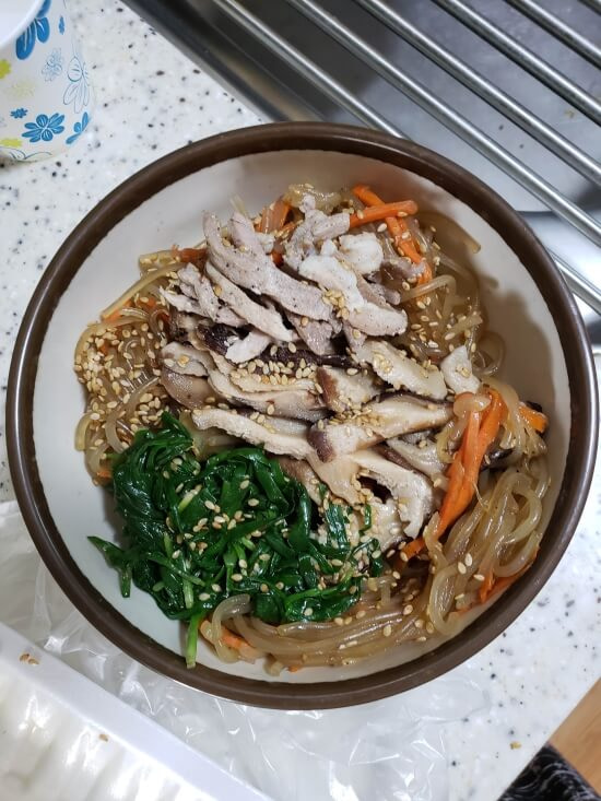 A bowl of japchae with toppings of veggies and meat