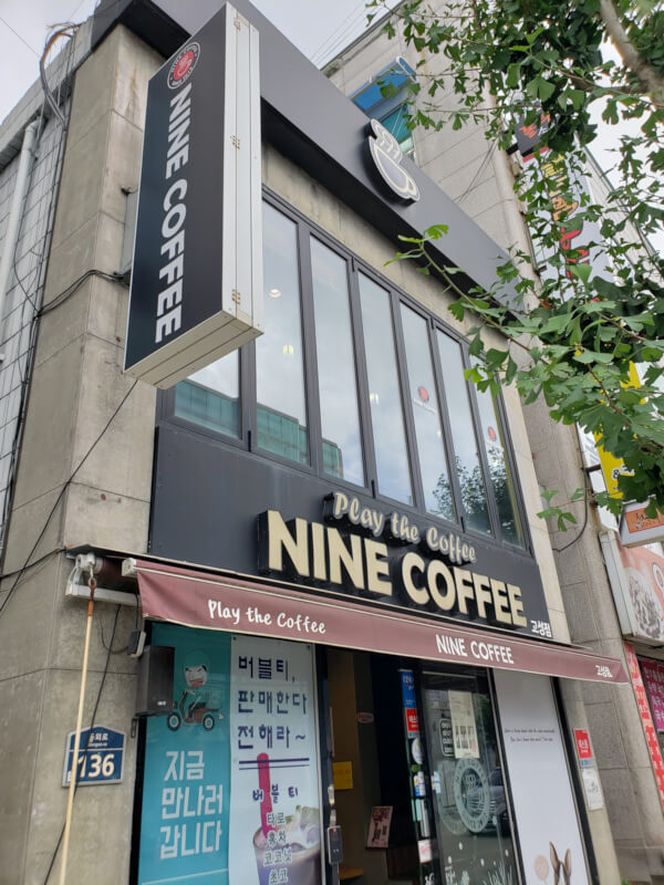 View of Nine Coffee from outside with a black sign and tall windows on second floor
