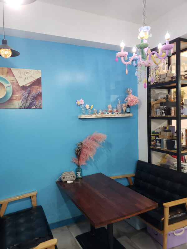 A table along a bright blue wall inside Dangdong Bakcine Coffee with a pink chandelier