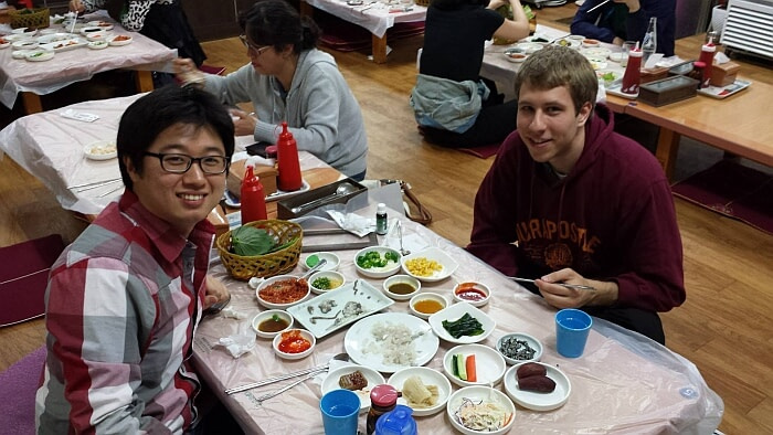 Nate with a friend sitting on the floor at a raw fish restaurant in South Korea
