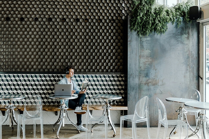 A man at an American café with a laptop and reading a book while listening to something