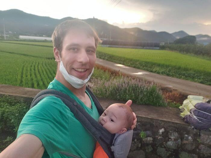 Nate walking down a country road along rice fields near Jangsan Forest with baby son Noah