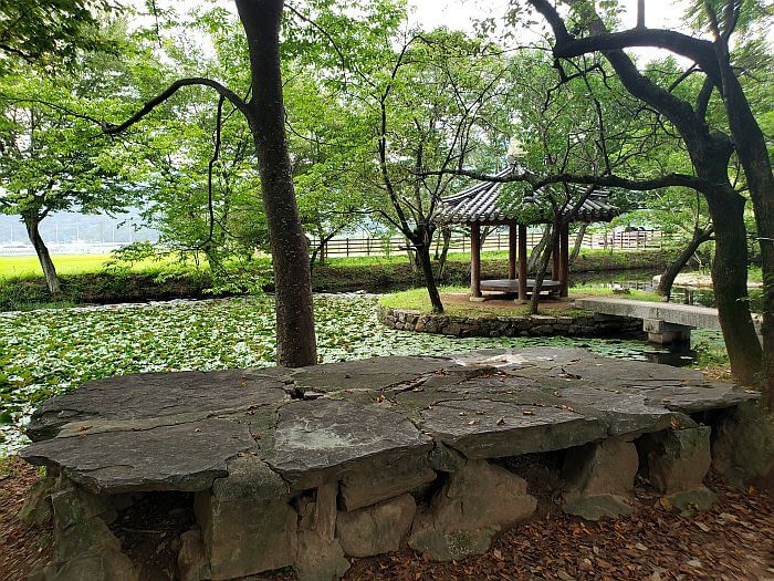 Rock table or memorial next to a pond with a gazebo in the middle in the forest
