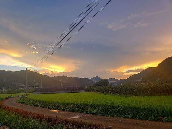 A sunset above mountains and a road along rice fields