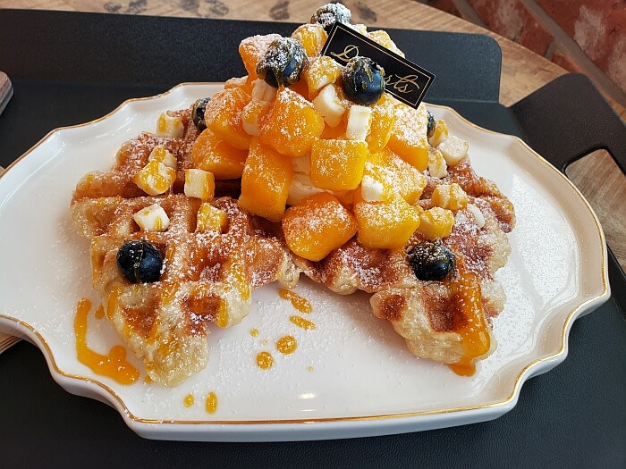 A mango cheese croffle topped with ice cream, blue berries, cheese, and powdered sugar