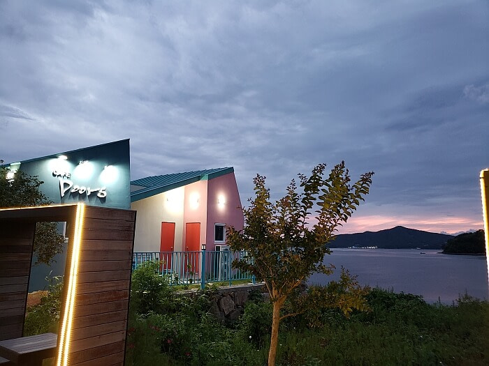 A smaller building with a Doors Café sign lit up at sunset