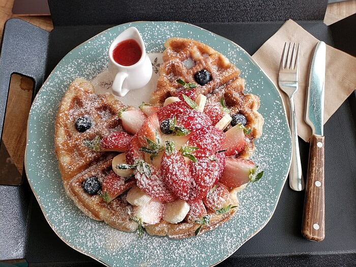 A strawberry ice cream croffle or waffle topped with ice cream, blue berries, bananas, and powdered sugar
