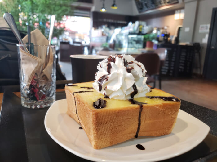 A plate of honey bread topped with chocolate syrup, whipped cream, and butter