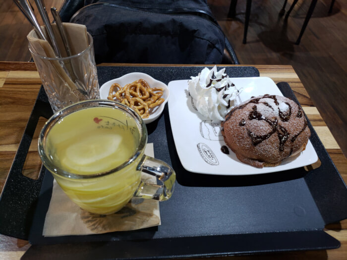 A tray with a mocha bun with a side of whip cream, pretzels, and citron tea