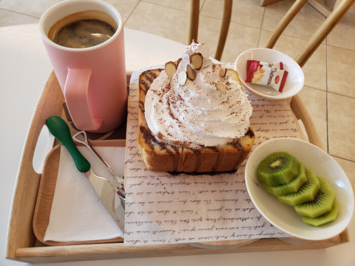 A tray of honey bread with whipped cream and cinnamon, kiwi, and coffee