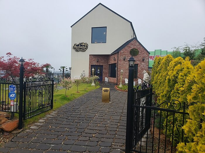 A black gate opened with a stone pathway leading to the café building with a courtyard on the left