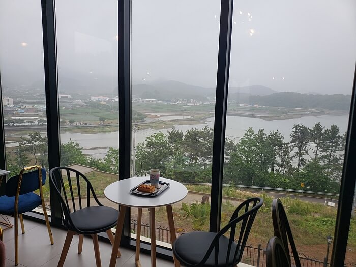 A pastry and coffee on a small table next to large windows with a nice view