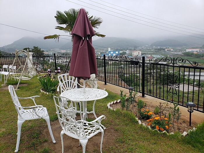 A white table and chairs along a railing with flowers overlooking a nice view of mountains and the town below