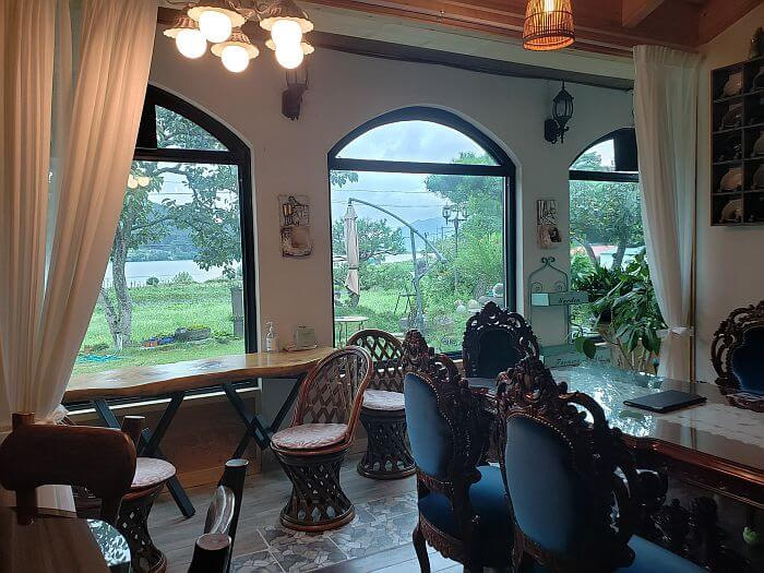 A long wooden table along some windows and some antique, Western style chairs