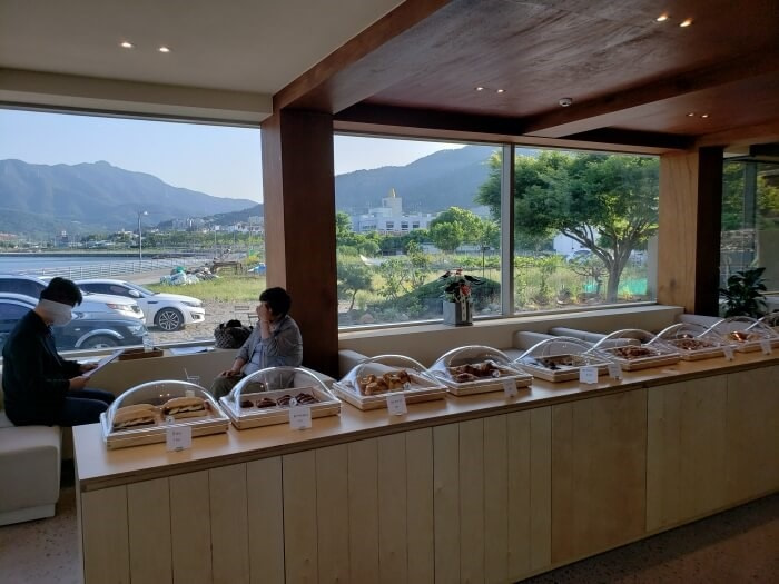 A row of pastries with plastic covers across from people seated along the window