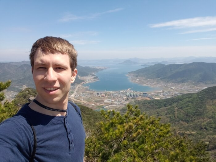 Nate on Georyusan peak with a view of the sea and outlying islands and mountains