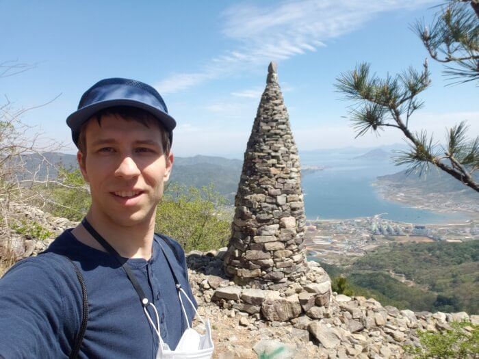Nate standing in front of a stone pagoda with a sea view in the background