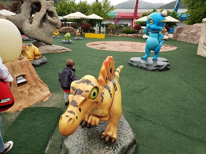 Noah walking between small dinosaur characters in the kids dinosaur area