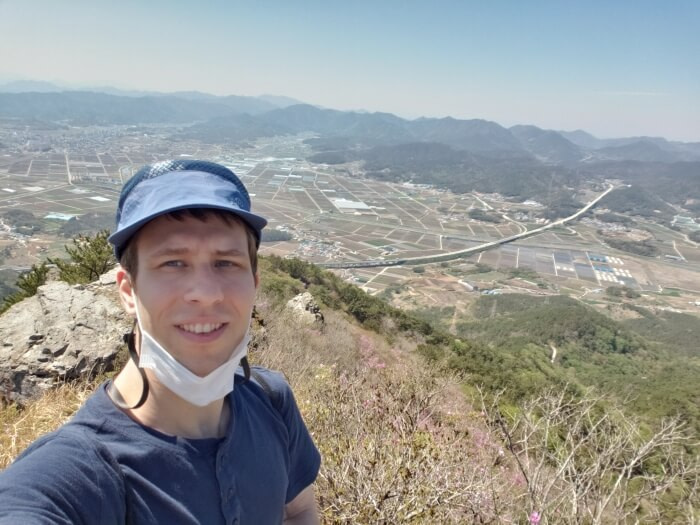 Nate standing in front of a view of his village without any zoom, showing the highway cutting across the town