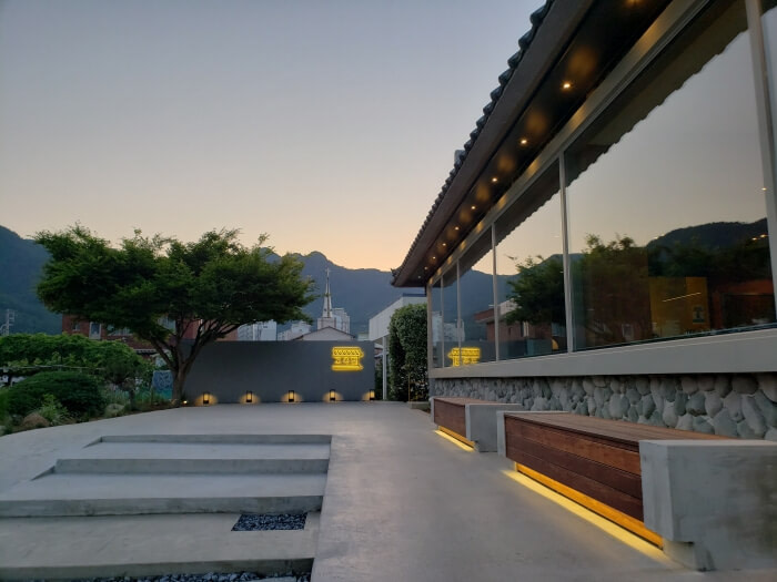 A few stairs leading to the entrance of Googjeong Café with lights illuminating benches outside along a window in the evening