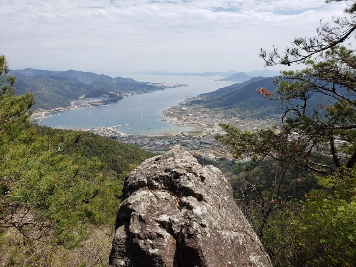 A large single rock jutting out in front of a nice view of the water and towns