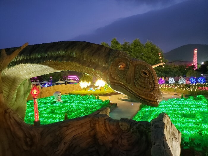 A long-necked dinosaur looking at the viewer at night with green lights below