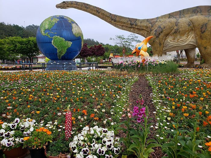 A long-necked dinosaur looming over a big globe next to a garden of flowers at the Goseong Dinosaur Theme Park
