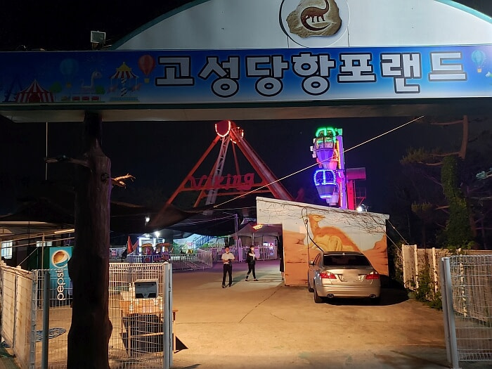Entrance to Danghangpo Land at night with a welcome sign overhead and Viking ride and Ferris wheel straight ahead