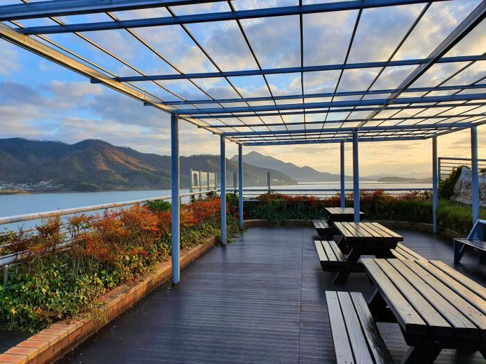 Setting sun shining on the mountains and picnic tables on top of a seaside cliff