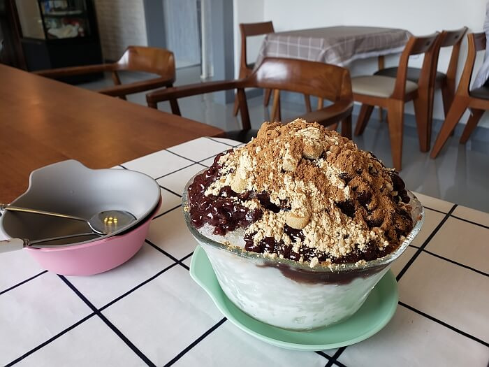 A bowl of pat-bingsu on a table with toppings of red bean, grain powder, and cinnamon