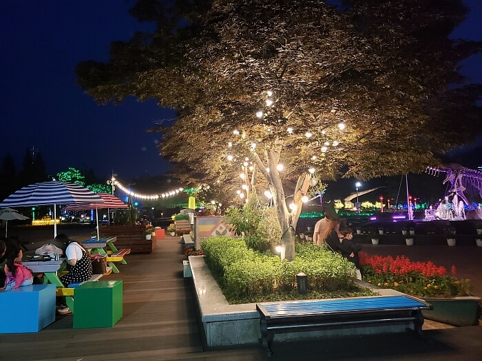 People sitting at picnic tables at night next to trees with lights and other plants and flowers
