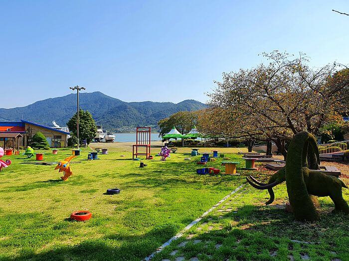 A tree and bush in the shape of an elephant next to the grassy playground with colorful items scattered around
