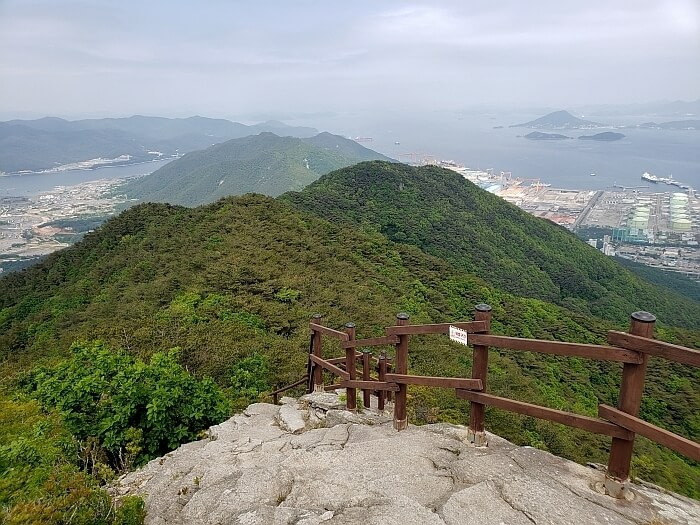 A wooden fence along a rocky slope with several peaks in the distance and villages along the sea below