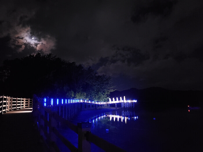 The moon shining over the boardwalk lit with blue lights reflecting off the water at night