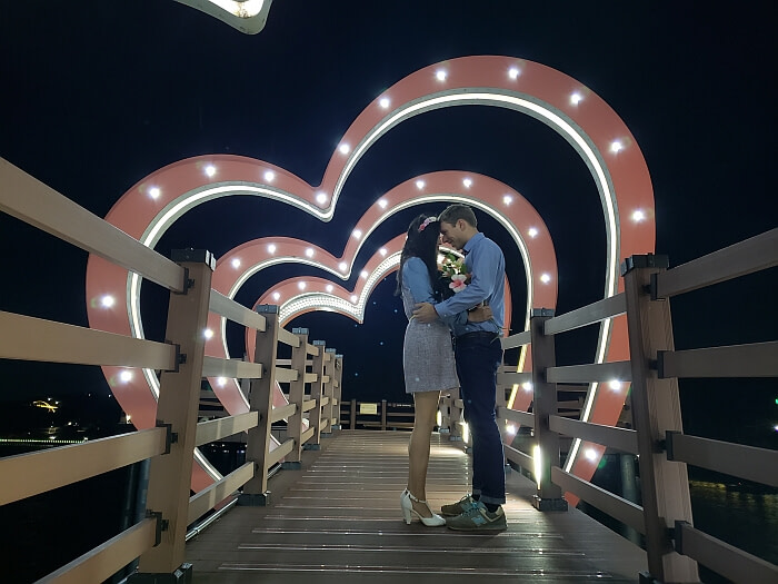 Nate and Alice embracing under heart-shaped arches lit up at night