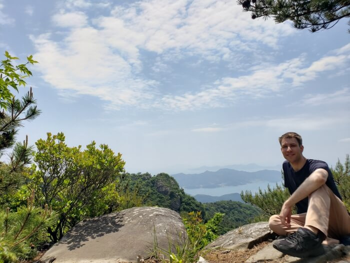 Nate sitting on a rocky ledge overlooking a view of other peaks and islands around the sea