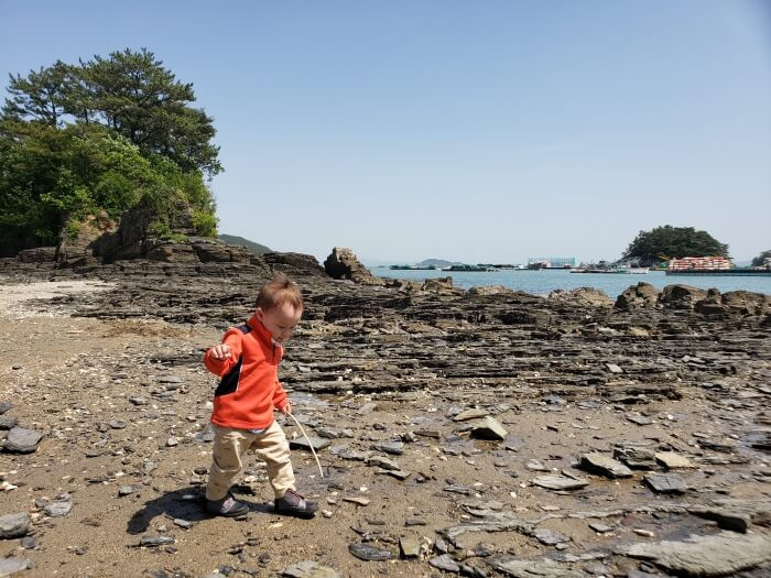 Noah walking along the rocky shore of Solseom Island with a stick