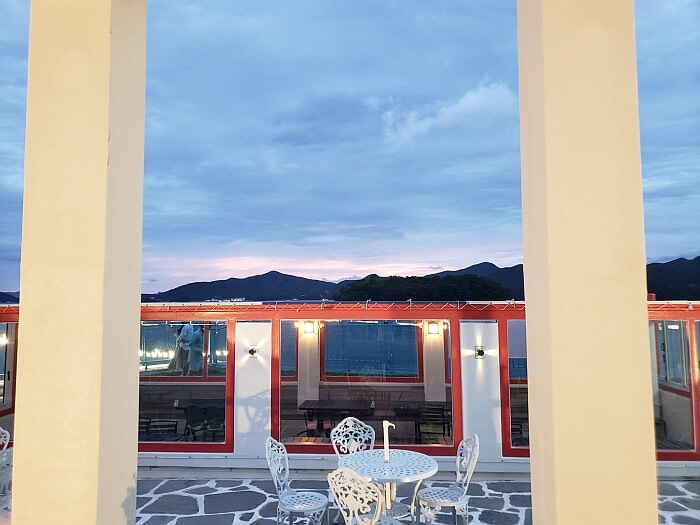 A white table and chairs between white columns and an enclosed seating area outside at sunset