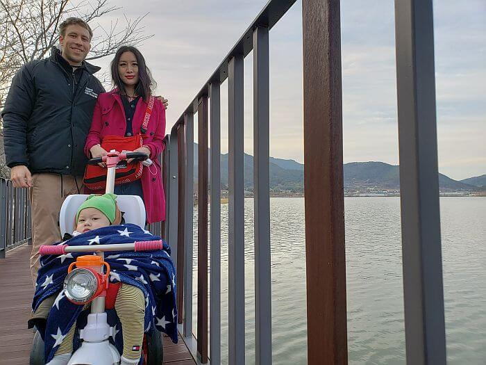 Family photo on the boardwalk along the water with Noah bundled up with a hat and blankets in the stroller