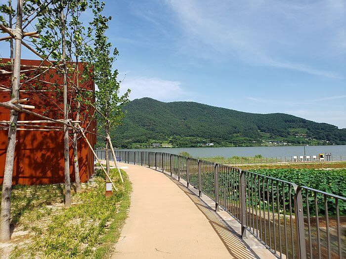 A paved path with a fence wrapping around the steel structures and the lotus pond below next to the reservoir