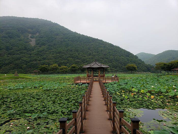 A bridge connecting to a gazebo in the middle of a pond surrounded by mountains