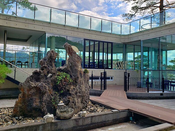 A large rock outside the café with trees growing through a large rooftop